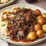Slow Cooker Sirloin Tip Roast with rich gravy, baby potatoes, and fresh herbs served over creamy mashed potatoes.
