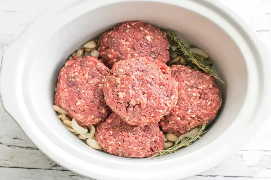 Raw patties prepared for Slow Cooker Salisbury Steaks on a bed of onions and thyme