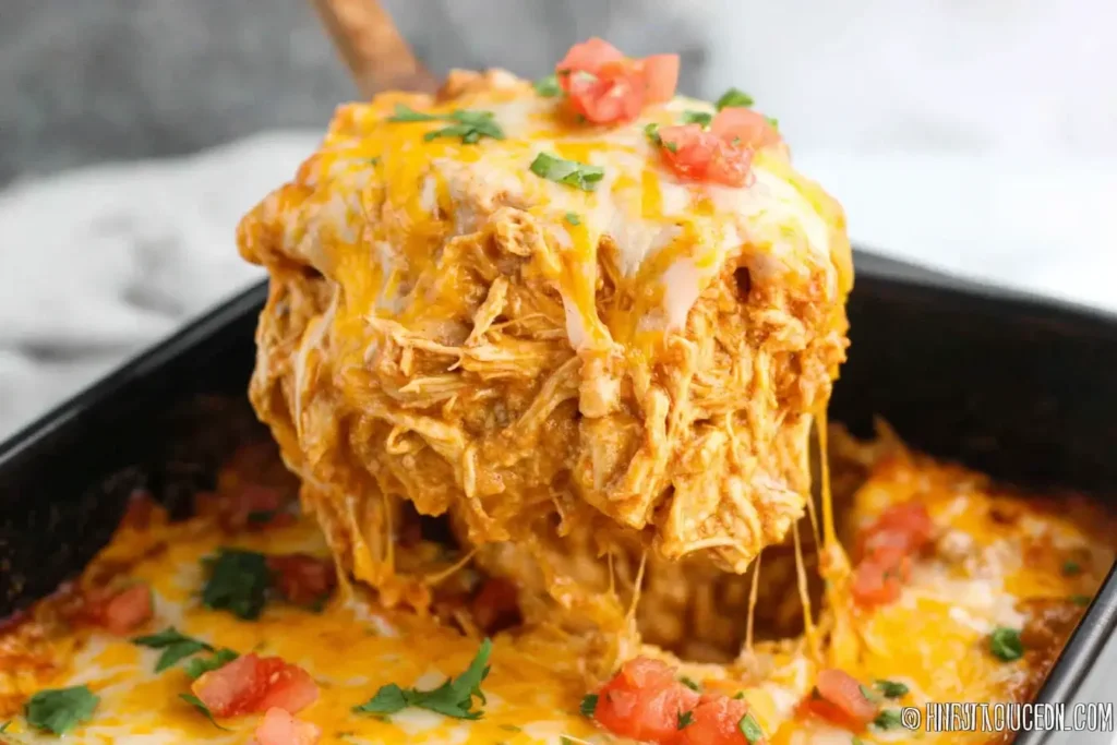 Cheesy serving of Slow Cooker Chicken Enchilada Casserole lifted from baking dish with melted cheese and tomatoes