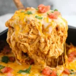Cheesy serving of Slow Cooker Chicken Enchilada Casserole lifted from baking dish with melted cheese and tomatoes