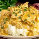 Crock Pot Chicken and Gravy served over creamy mashed potatoes, topped with fresh parsley