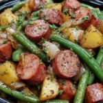 Crockpot Kielbasa and Green Beans with potatoes and onions, seasoned and served in a black dish.