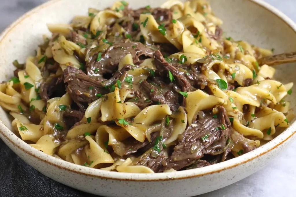 Crock Pot Beef and Noodles with tender shredded beef, egg noodles, and rich gravy served in a rustic bowl.
