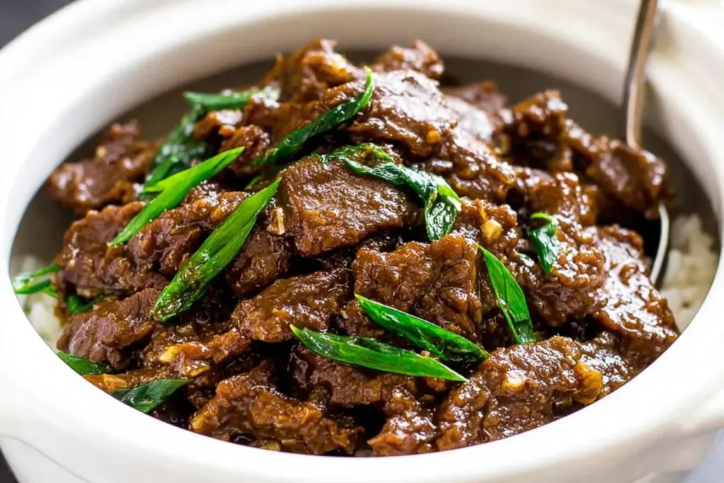 Slow Cooker Mongolian Beef served over rice with green onions in a white bowl.