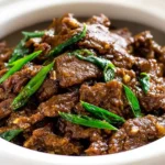 Slow Cooker Mongolian Beef served over rice with green onions in a white bowl.