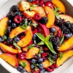 Fresh Summer Peach Fruit Salad with peaches, cherries, blackberries, blueberries, and basil in a white bowl.