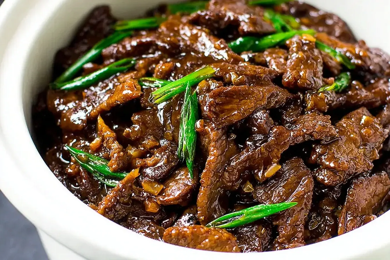 Tender beef strips in savory sauce with green onions – Slow Cooker Mongolian Beef served in a white bowl.