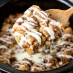 Close-up of Crock Pot Cinnamon Roll Casserole with icing being served from a slow cooker