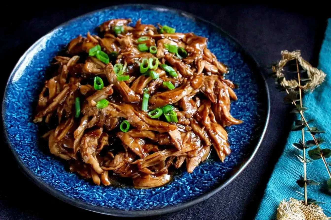 Slow Cooker Hoisin Chicken served shredded on a blue plate, garnished with sliced green onions.