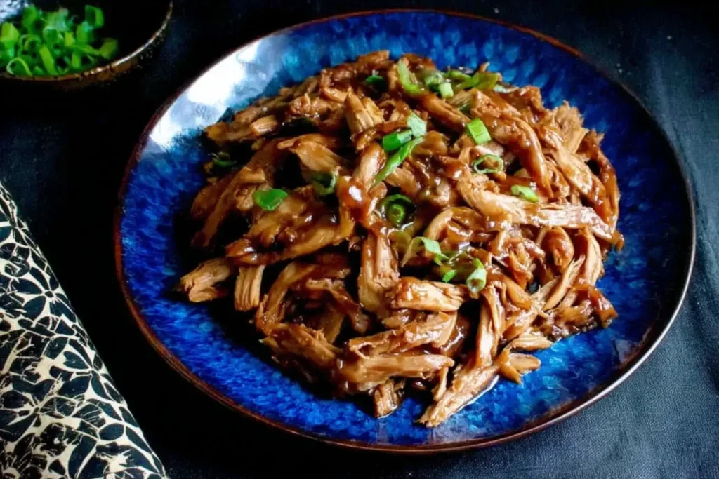 Shredded Slow Cooker Hoisin Chicken topped with green onions, served on a vibrant blue plate.