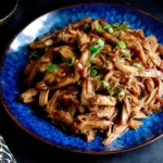 Shredded Slow Cooker Hoisin Chicken topped with green onions, served on a vibrant blue plate.