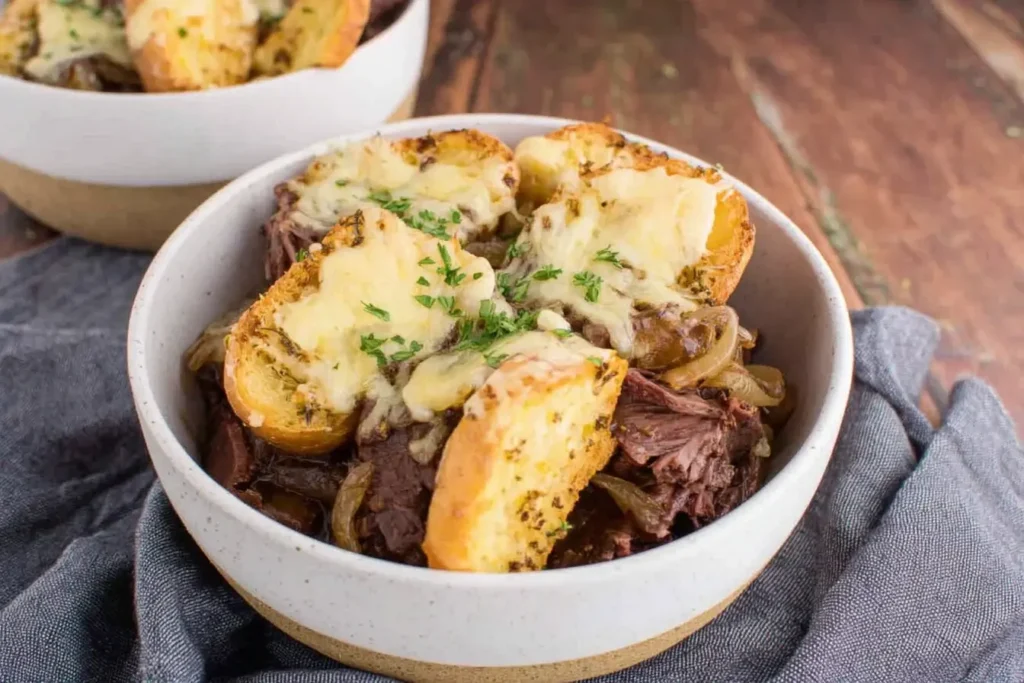 Bowl of French Onion Pot Roast topped with cheesy baguette slices and garnished with fresh herbs.