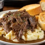 Slow Cooker Beef Manhattan with shredded beef and brown gravy over mashed potatoes, served with toasted bread slices.