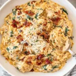 Slow Cooker Creamy Tuscan Chicken Orzo served in a white bowl, topped with Parmesan, crispy bacon, and fresh herbs.