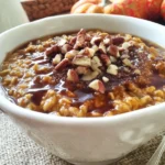 Slow Cooker Pumpkin Maple Oatmeal topped with chopped pecans and maple syrup in a white bowl