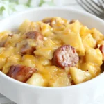 Bowl of Slow Cooker Sausage and Potato Casserole with creamy cheese and sliced kielbasa on a rustic wooden table.