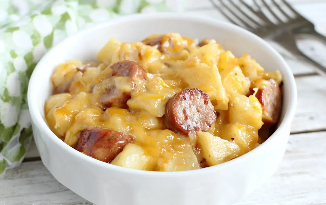 Bowl of Slow Cooker Sausage and Potato Casserole with creamy cheese and sliced kielbasa on a rustic wooden table.