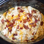 Keto Crack Chicken in the Crock Pot topped with crispy bacon and melted cheddar cheese in a slow cooker.