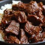 Slow Cooker Korean Beef with tender chunks of beef in rich sauce served over white rice in a black bowl.