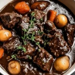 Slow Cooker Beef Bourguignon with tender beef chunks, carrots, and baby potatoes in a rich wine sauce, served in a white bowl.