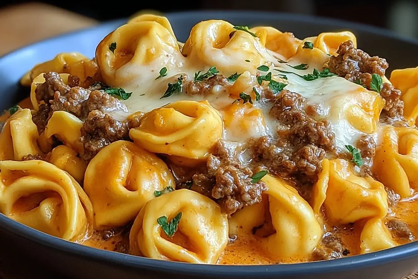 Cheesesteak Tortellini topped with melted provolone cheese and ground beef in a creamy sauce, garnished with fresh parsley.