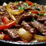 Chinese Pepper Steak with Onions served sizzling in a cast-iron skillet with tender beef, caramelized onions, and sweet red peppers in savory sauce.