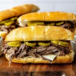 Slow Cooker Italian Beef Sandwiches served on toasted hoagie rolls with melted cheese, tangy pepperoncini, and au jus dipping sauce.