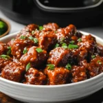 A bowl of slow cooker General Tso’s Chicken topped with sesame seeds and green onions, served with rice and broccoli.