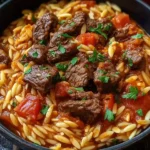 Hearty Beef Giouvetsi with tender beef chunks and orzo pasta in rich tomato sauce, garnished with fresh parsley in a black bowl.