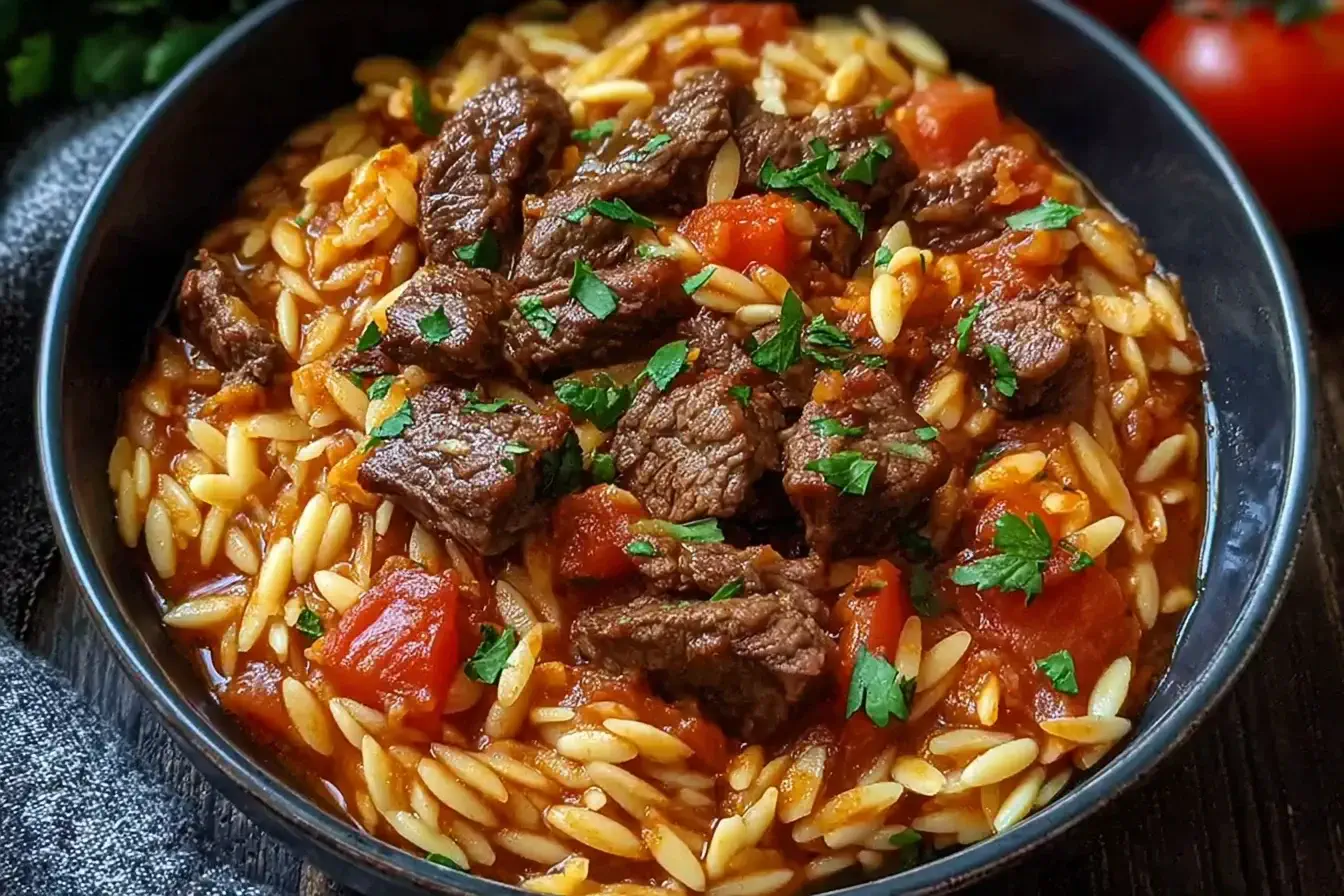 Hearty Beef Giouvetsi with tender beef chunks and orzo pasta in rich tomato sauce, garnished with fresh parsley in a black bowl.