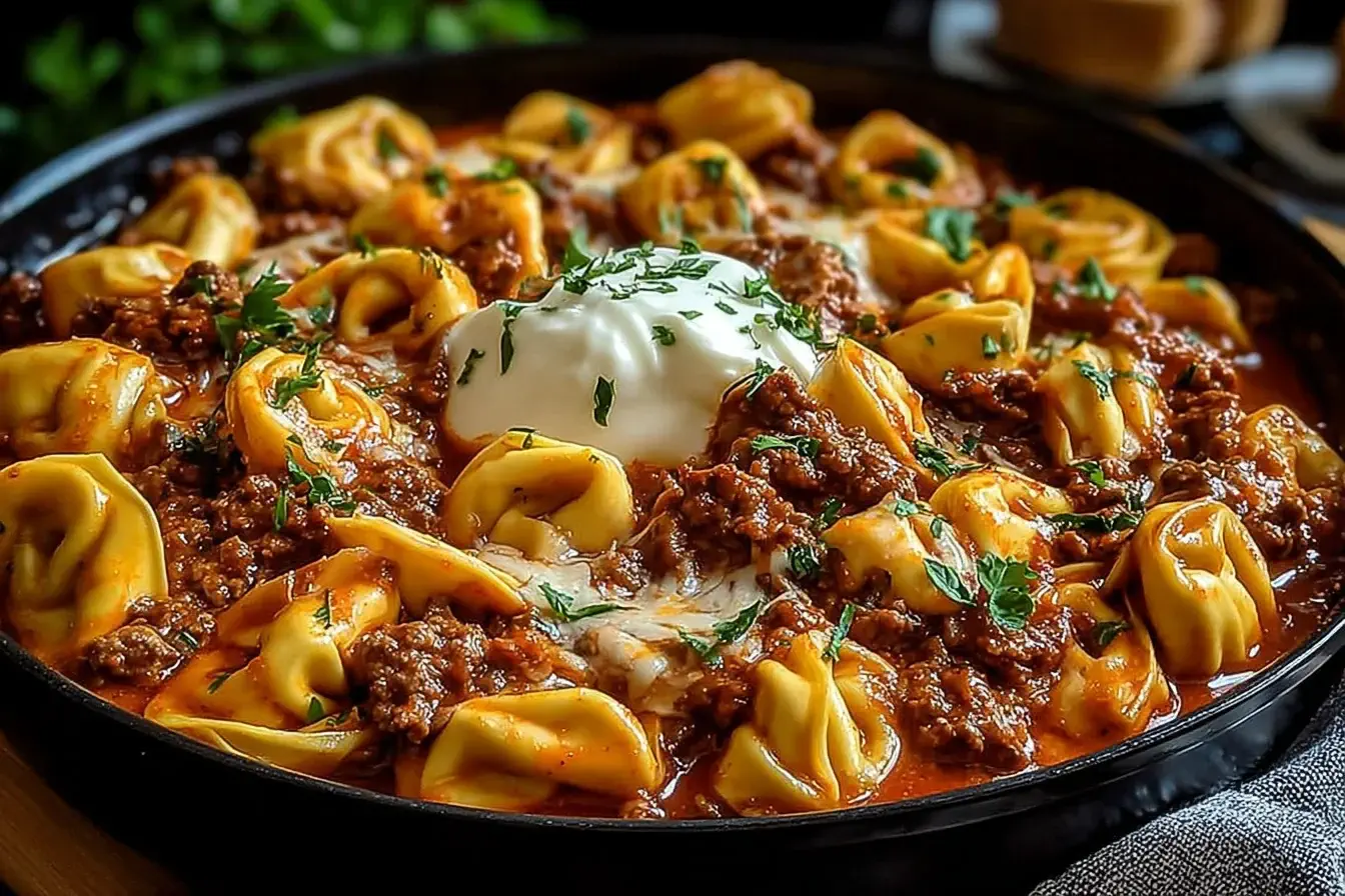 Cheesy Beef Enchiladas Tortellini in a skillet topped with sour cream and fresh herbs.