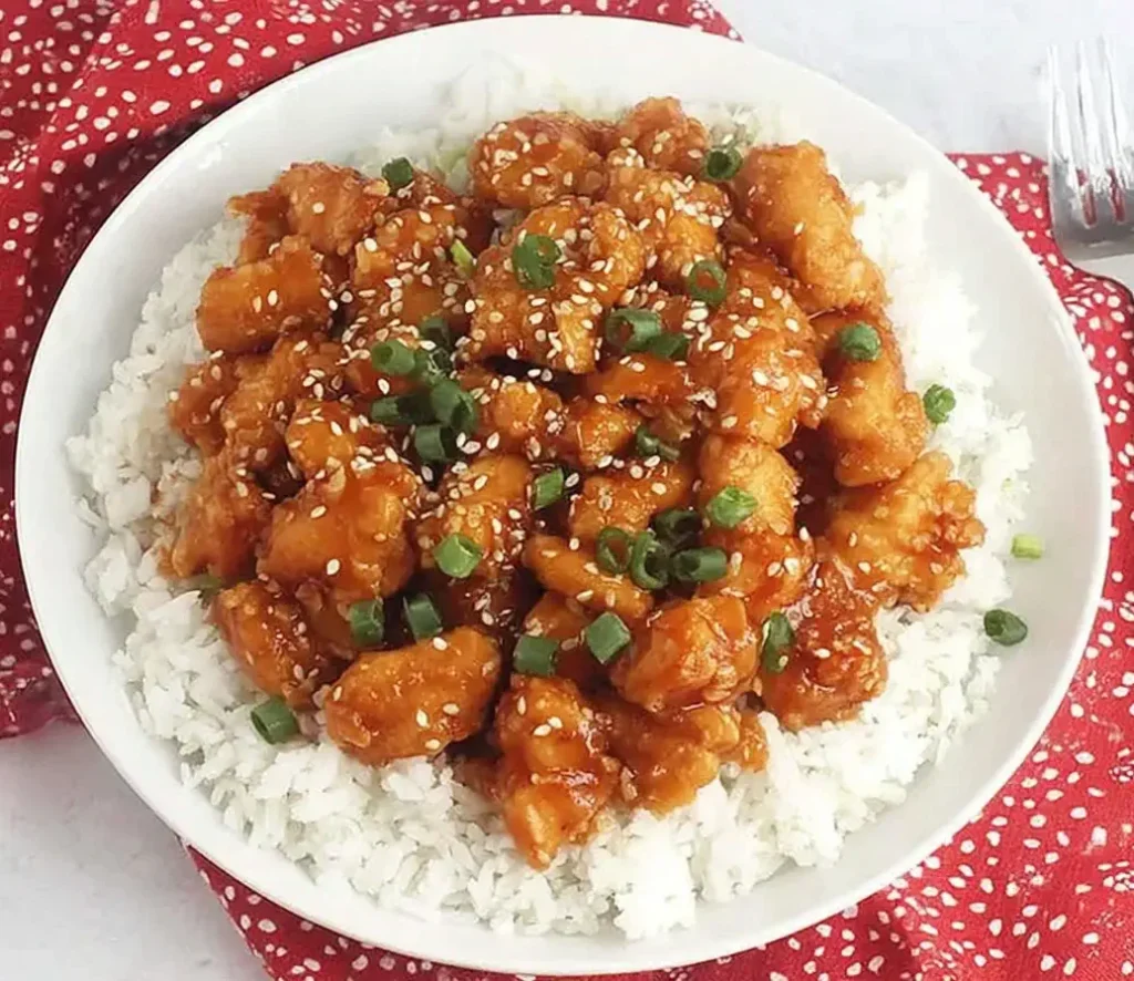 Crockpot Sweet and Sour Chicken served on fluffy white rice, garnished with sesame seeds and chopped green onions.