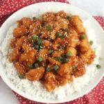 Crockpot Sweet and Sour Chicken served on fluffy white rice, garnished with sesame seeds and chopped green onions.
