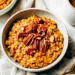 Close-up of Slow Cooker Pumpkin Pie Oatmeal topped with glazed pecans and served with coffee in a speckled mug.