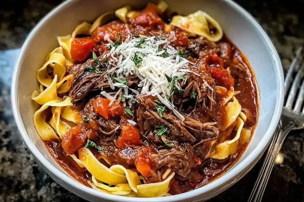 Close-up of Sunday Slow Cooker Beef Ragu served over ribbon pasta, topped with fresh herbs and shredded Parmesan.