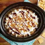 CrockPot S'mores Cake topped with marshmallows, graham crackers, and chocolate drizzle in a slow cooker.