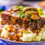 Slow Cooker Smothered Steak topped with mushroom gravy and fresh herbs, served over mashed potatoes.