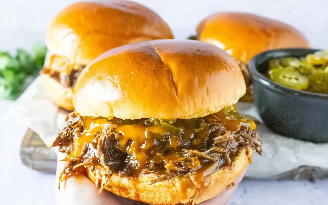 Slow Cooker Cowboy Sandwiches with shredded beef, cheese, and jalapeños on a toasted bun.