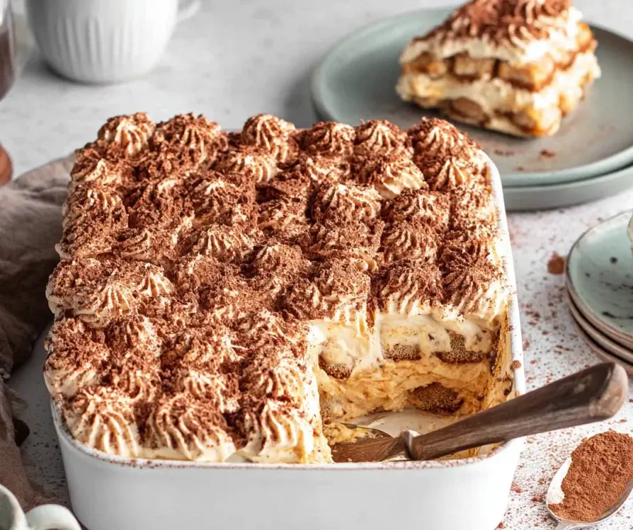 Creamy Pumpkin Tiramisu dessert layered with mascarpone, pumpkin spice, and cocoa powder in a white baking dish.