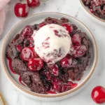 Slow Cooker Chocolate Cherry Dump Cake topped with vanilla ice cream and juicy cherries on a white plate.