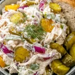 Savory Dill Pickle Chicken Salad with shredded chicken, pickles, and colorful vegetables served with bread and extra pickles.