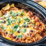 Crockpot Chicken Enchilada Casserole topped with melted cheese, black beans, and fresh cilantro in a slow cooker.