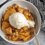 Apple Crisp Crockpot served warm in a bowl with vanilla ice cream and oat crumble topping.