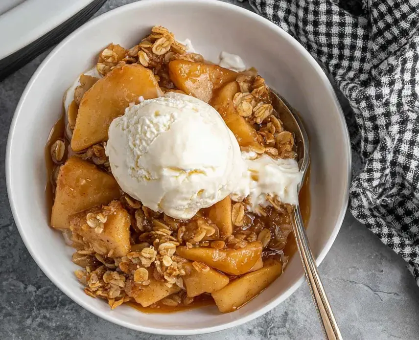 Apple Crisp Crockpot served warm in a bowl with vanilla ice cream and oat crumble topping.