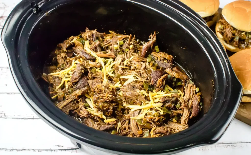 Slow Cooker Cowboy Sandwiches beef filling with shredded chuck roast, jalapeños, and cheese in a crockpot.