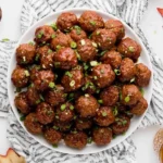 Slow Cooker Apple Butter Meatballs served on a white plate, topped with chopped green onions, surrounded by apples and a fall leaf