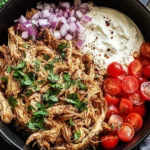 Shredded slow cooker chicken shawarma served with fresh tomatoes, red onions, parsley, and creamy yogurt sauce in a black bowl.