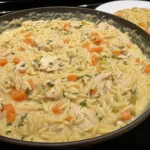 Creamy Chicken Pot Pie Orzo in a skillet with carrots, chicken, and herbs.