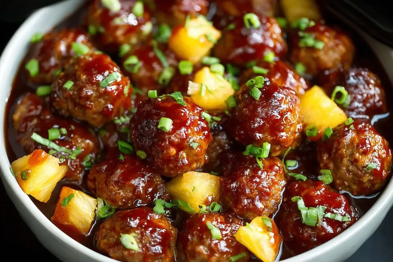Slow Cooker Pineapple Barbecue Meatballs Recipe Slow Cooker Pineapple Barbecue Meatballs coated in tangy barbecue sauce with pineapple chunks and green onions served in a white bowl.
