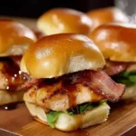 Maple Chicken and Beef Bacon Sliders stacked on a wooden board, glazed with maple syrup and layered with crispy beef bacon and fresh greens.